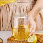 Vertiendo aceite dorado en botella dispensadora de vidrio transparente. Limón a un lado sobre base de madera.