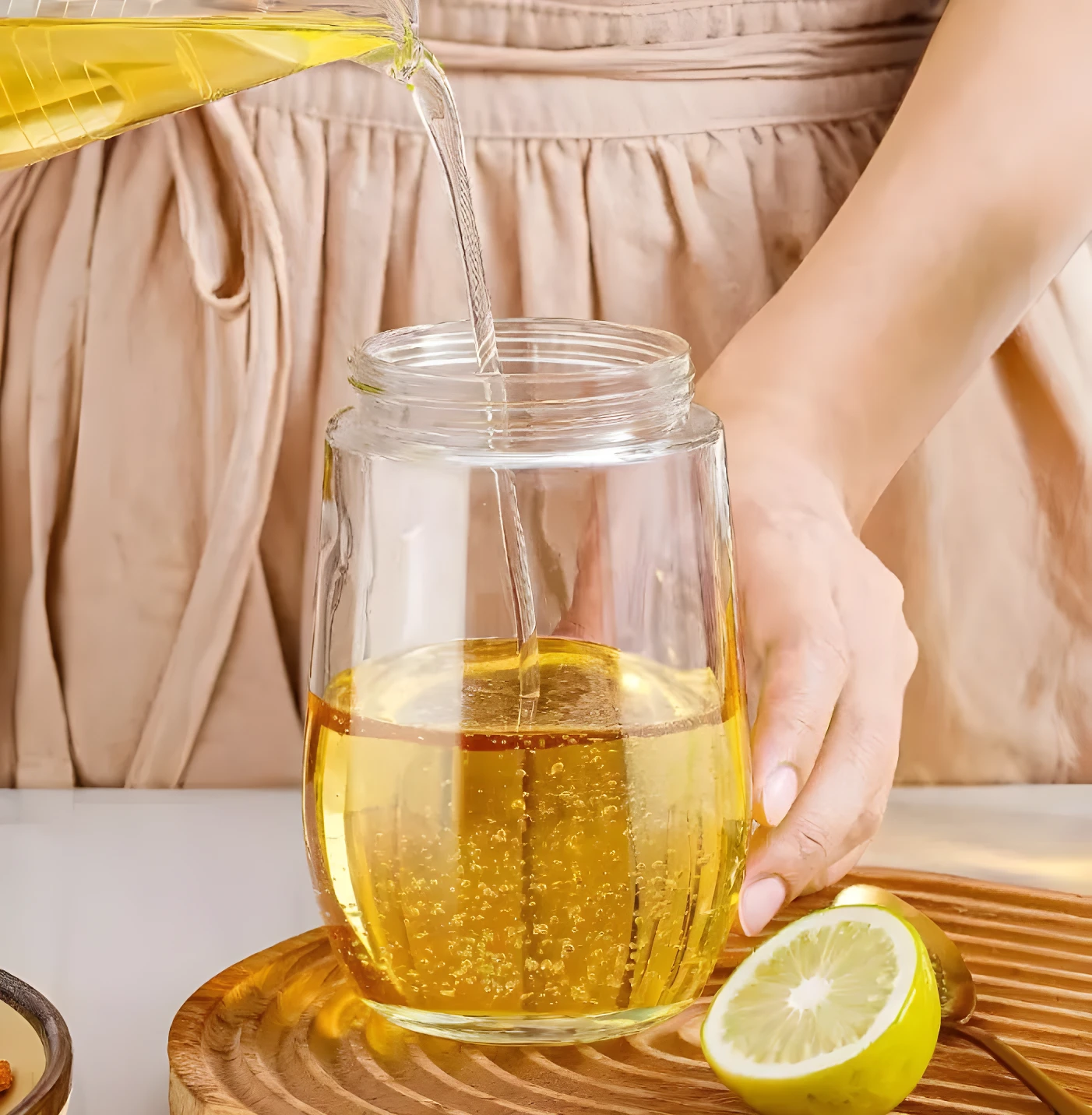 Vertiendo aceite dorado en botella dispensadora de vidrio transparente. Limón a un lado sobre base de madera.