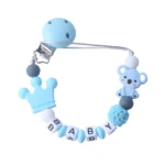 Sujetador de chupete azul claro de silicona con clip, dije de corona, koala y cuentas con letras que forman "BABY".