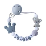 Cadena sujeta chupete bebé silicona gris y blanco con clip, dije corona, koala y cuentas deletreando "BABY".