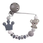 Cadena sujetachupetes de silicona gris y blanco con clip, dije de corona y koala, y cuentas con letras que forman "BABY".