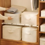 Cajas organizadoras de tela beige con asas, una abierta mostrando ropa doblada.