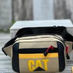 Riñonera Caterpillar color beige con logo amarillo, ideal para uso casual y outdoor.