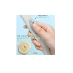 Mano presionando botón de cepillo facial gris para producir burbujas, exfoliación suave de la piel.