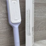 Cepillo peine retráctil lavanda con cerdas blancas para limpieza automática de cabello.