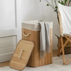Cesta de ropa sucia de bambú con forro y tapa, con manta gris y silla de madera al lado.