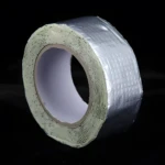 Rollo de cinta butilo impermeable plateada, canto expuesto con adhesivo grueso en capas sobre cartón central.