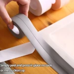 Mano aplicando cinta de sellado gris, impermeable y autoadhesiva, sobre el borde de una superficie blanca, sin necesidad de herramientas.