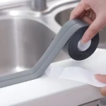 Aplicación de cinta selladora impermeable gris autoadhesiva en el borde de un lavaplatos de acero inoxidable.