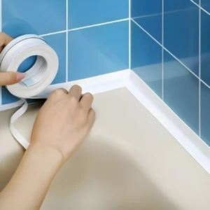 Aplicación de cinta selladora blanca impermeable de 32 mm en la esquina entre azulejo azul y superficie beige.
