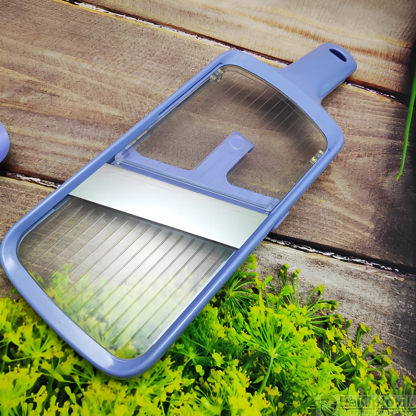 Mandolina cortadora de vegetales azul lavanda con cuchilla de acero expuesta, sobre fondo rústico de madera y hojas de eneldo.