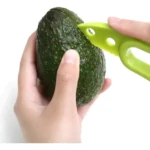 Manos cortando cáscara de aguacate Hass texturizado con herramienta verde lima, pelador multifuncional.