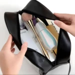 Cosmetiquera Washbag negra abierta, con brochas y envases de productos de belleza, manos organizando.