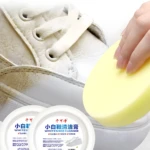 Persona limpiando zapato blanco con esponja amarilla y crema blanqueadora.