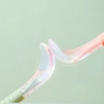 Cucharas de silicona flexibles para bebé, una verde y otra rosa, mostrando su capacidad de doblarse y textura con cuadrícula roja.