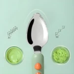 Cuchara de metal y mango verde para bebé, cabeza con bordes dentados para raspar purés verde claro y verde texturizado.