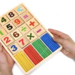 Set didáctico de madera con números, operadores matemáticos y palitos contadores de colores (amarillo, rojo, verde y azul) sostenido por manos.