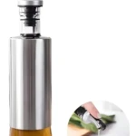 Dispensador de aceite V160 vidrio y acero inoxidable con vertedor que gotea aceite en un tazón pequeño.