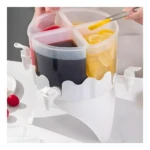 Dispensador giratorio blanco para bebidas con cuatro compartimentos; uno con limonada y otro con bebida oscura.