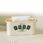 Dispensador de pañuelos color crema con tapa de madera y diseño "GOOD" en verde.