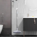 Escoba raspador de silicona blanca y gris con mango metálico, colgada en pared de baño moderno.