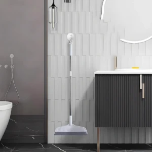 Escoba raspador de silicona blanca y gris con mango metálico, colgada en pared de baño moderno.