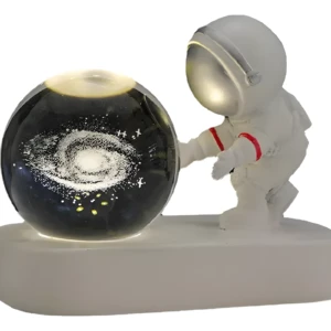 Lámpara de resina astronauta junto a esfera con galaxia, emite luz suave.