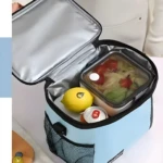 Lonchera térmica azul con interior plateado, contiene ensalada, limón y lata.