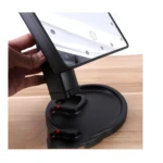 Espejo de maquillaje negro con base redonda y luces LED integradas, sujeto con mano.