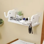 Estante organizador blanco con soportes de elefante sosteniendo gafas, reloj, audífonos, celular y llaves junto a planta decorativa.