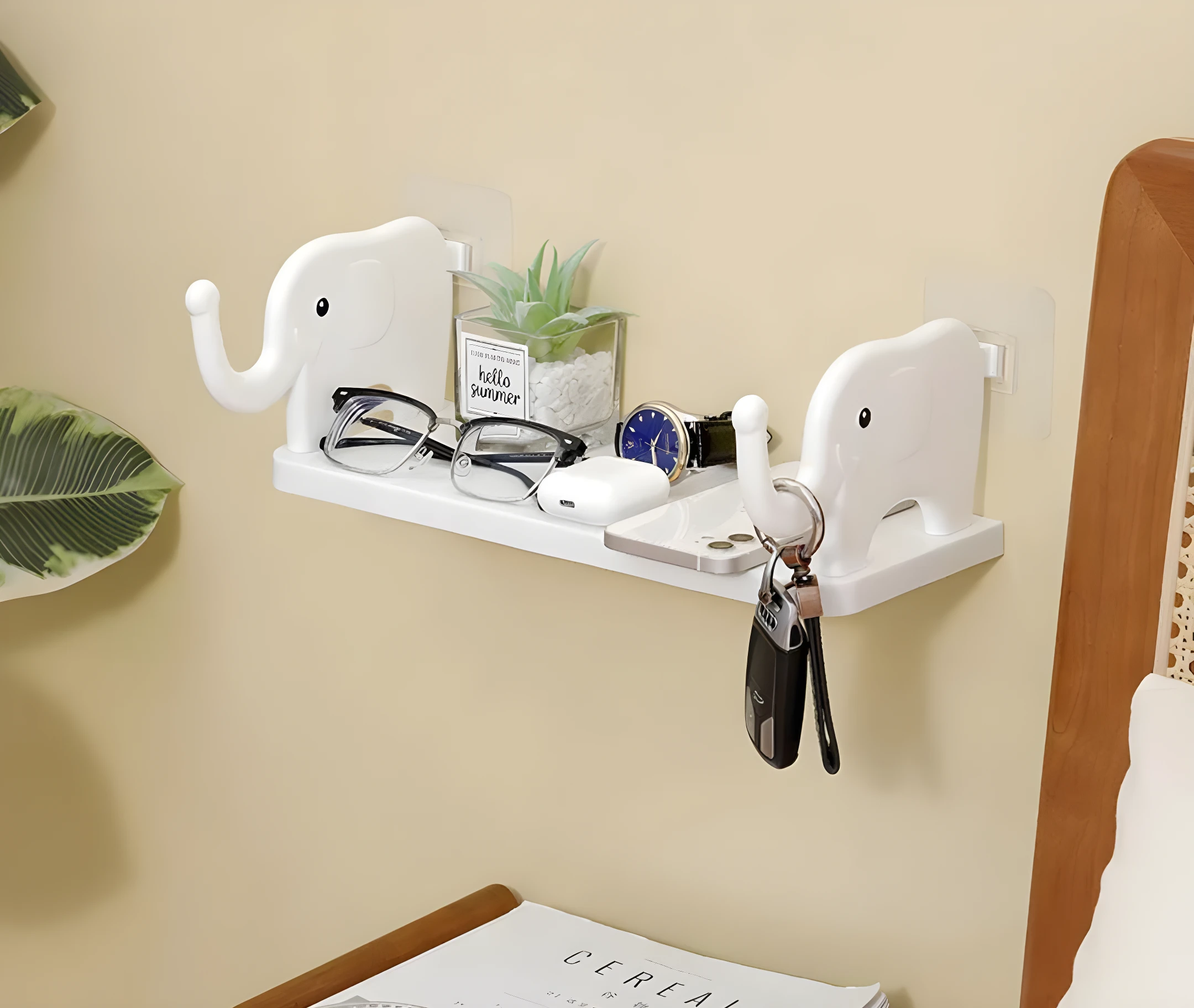 Estante organizador blanco con soportes de elefante sosteniendo gafas, reloj, audífonos, celular y llaves junto a planta decorativa.