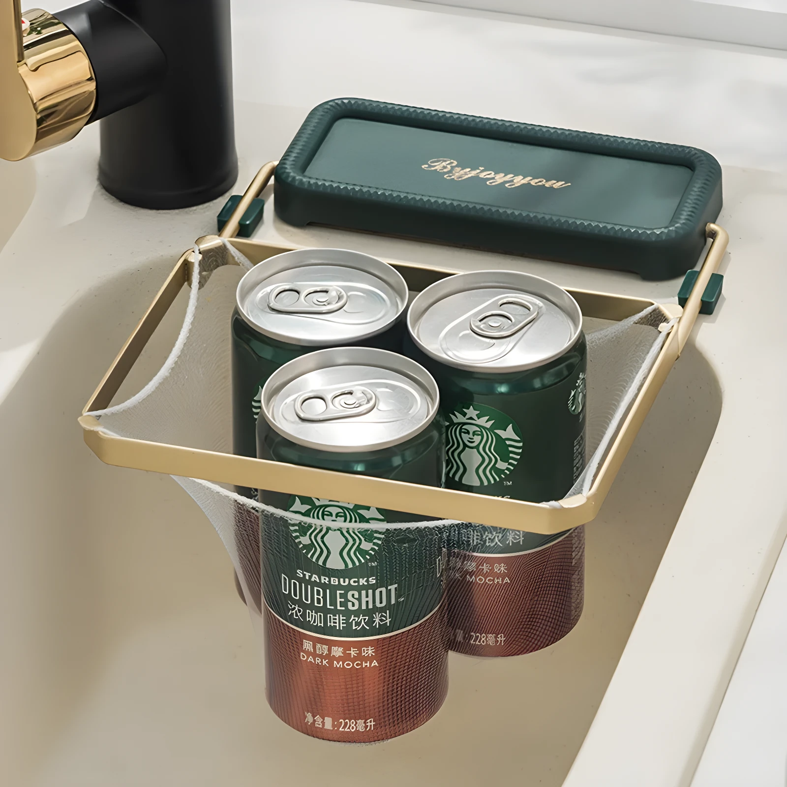 Estante esquinero dorado para fregadero con malla fina, sostiene latas de café Starbucks Dark Mocha.