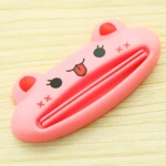 Exprimidor de pasta dental rosa con cara de animal feliz, sobre madera.