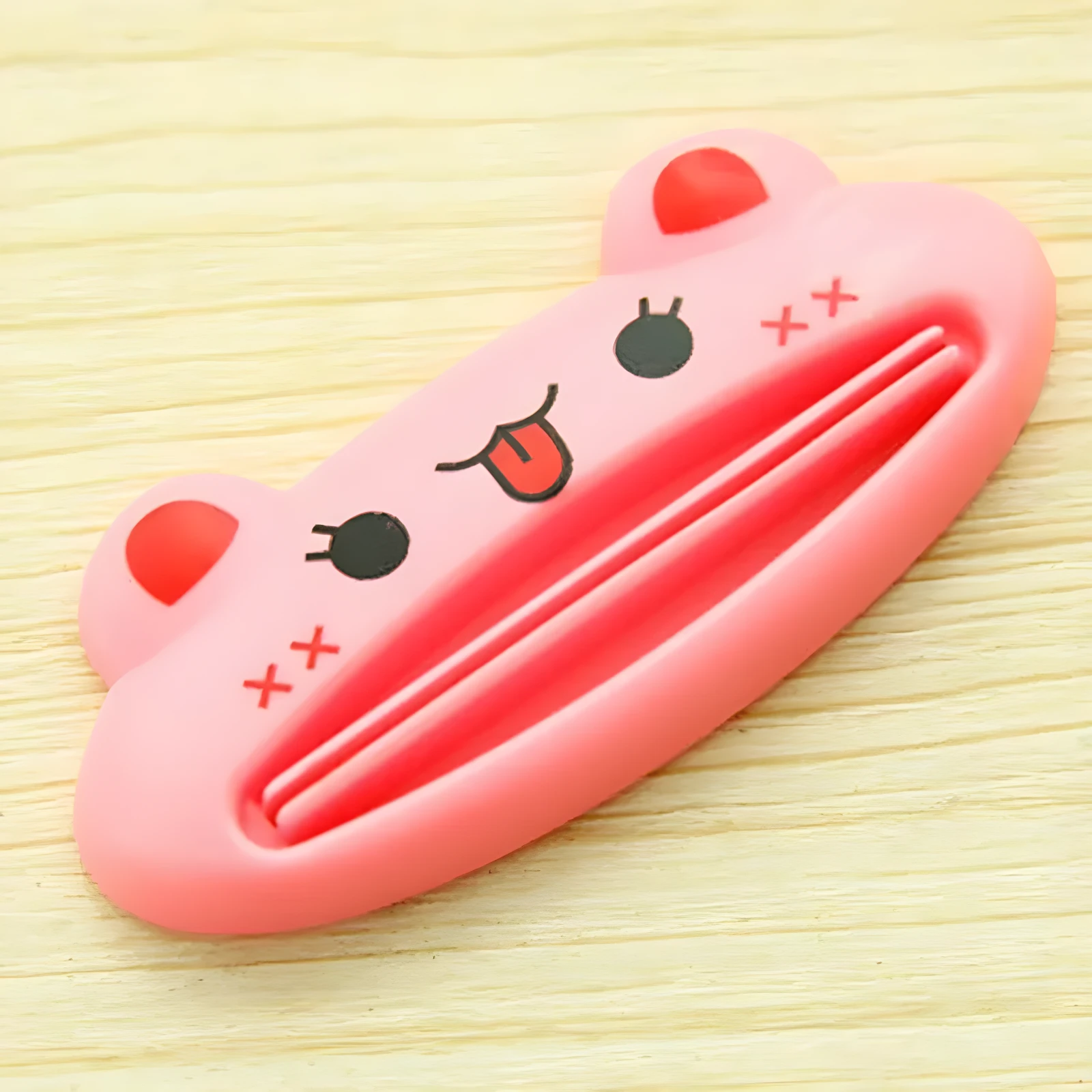 Exprimidor de pasta dental rosa con cara de animal feliz, sobre madera.