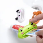 Exprimidor de pasta dental verde con forma de rana, sujetando un tubo, con dispensadores de panda y oso al fondo.