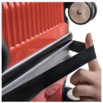 Mano estirando correa elástica negra sobre maleta de viaje roja brillante con textura acanalada.