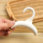 Gancho organizador blanco tipo arco con percha para bolsos, sostenido por mano sobre superficie de madera.