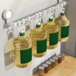Organizador de pared con ventosa fuerte: barra blanca con ganchos sosteniendo cuatro garrafas grandes de aceite y frascos de especias abajo.
