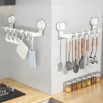 Organizadores de pared blancos con ventosa fuerte, exhibiendo tazas, paños, rallador, espátulas y cucharas de cocina en pared de azulejos grises.