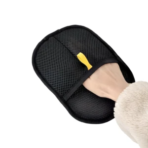 Mano enguantada con textura de borrego sosteniendo un guante cepillo negro de malla transpirable para mascotas, mostrando sujeta fácil amarilla.