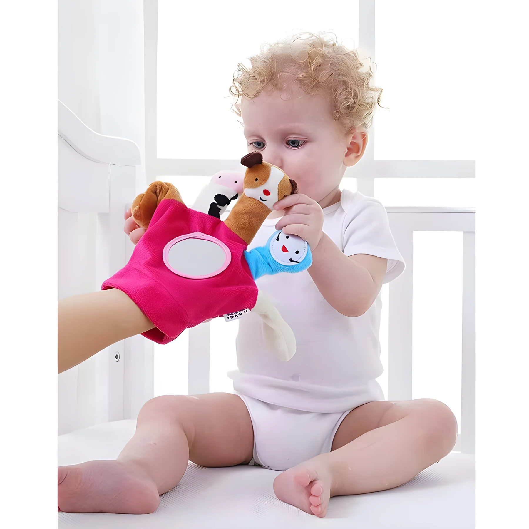 Bebé rubio en cuna blanca interactuando con guante de títere rosa con espejo y cabeza de caballo de peluche.