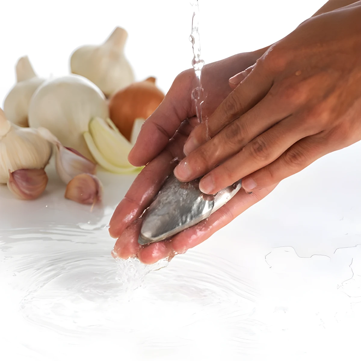 Manos lavan jabón metálico desodorizante bajo chorro de agua, con ajos y cebollas de fondo.