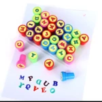 Sellos de abecedario de colores vibrantes, letras en goma y cuerpos plásticos, sobre papel blanco con algunas letras estampadas.