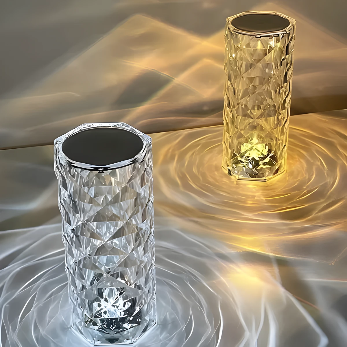 Dos lámparas de cristal facetado sobre superficie, una emite luz cálida dorada y la otra luz blanca fría, proyectando patrones ondulados.