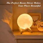 Lámpara de luna brillante sobre base de madera en mesa de noche con luz cálida, al lado de un despertador y un cuadro.