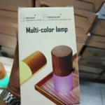 Lámpara de mesa cilíndrica con base de madera oscura, mostrando luz nocturna amarilla y modo multicolor púrpura.