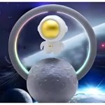 Astronauta blanco con casco dorado flotando en un aro, sobre una luna texturizada. Lámpara LED y altavoz.