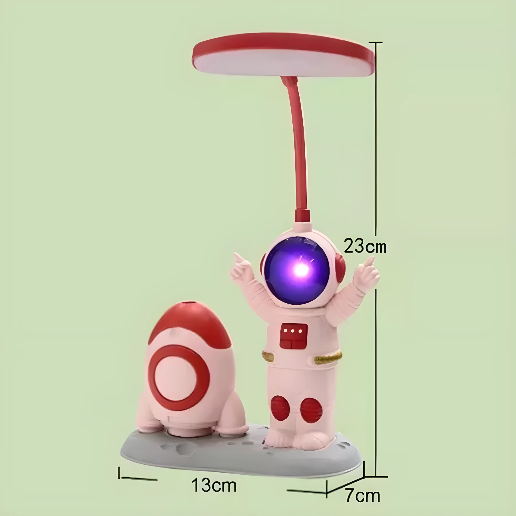 Lámpara de escritorio recargable con base gris y figuras de astronauta iluminado y cohete, color rosa y rojo. Alto 23cm, ancho 13cm.