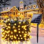 Guirnalda de luces solares navideñas amarillas de 3 metros iluminando jardín nevado y casas decoradas.
