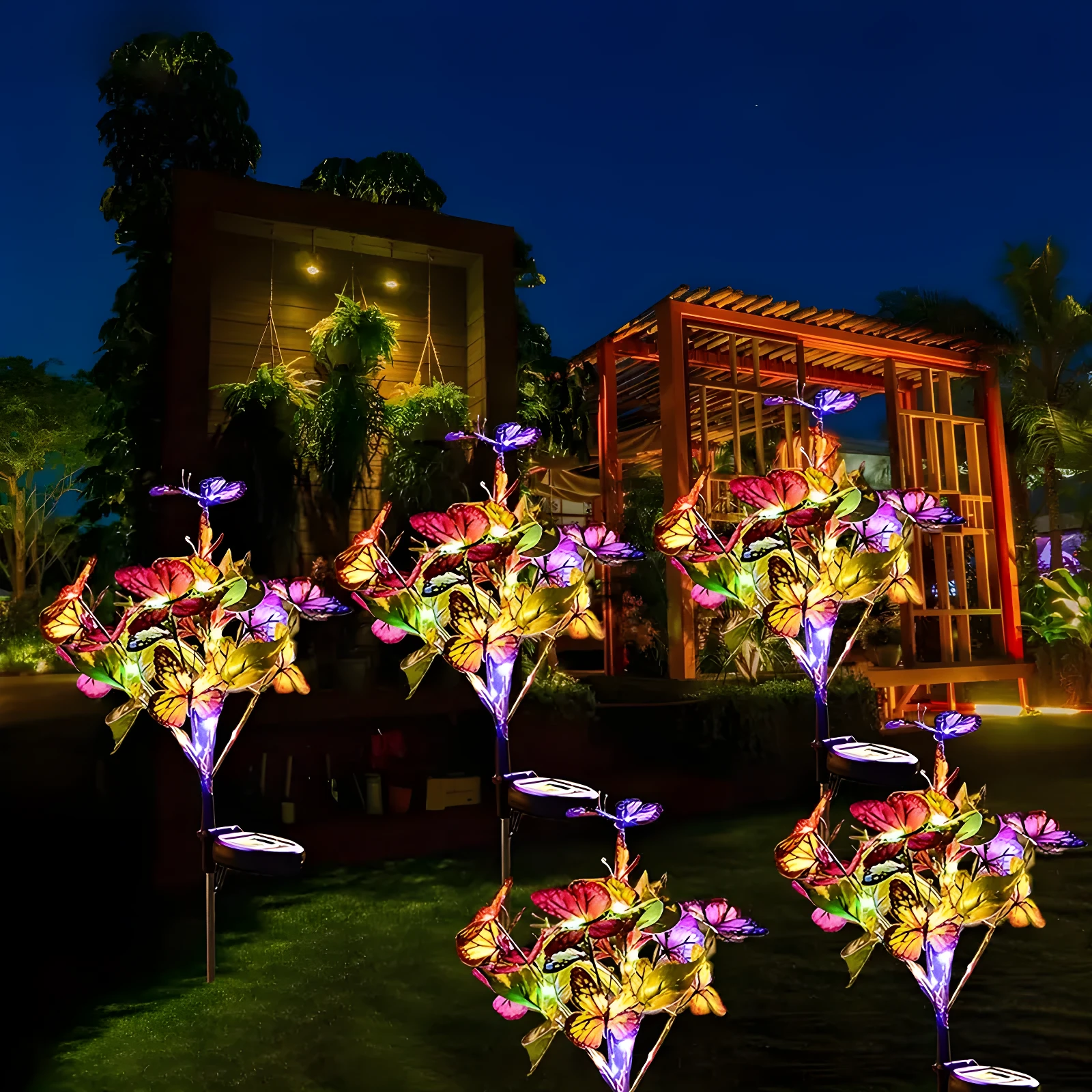 Lámparas solares de jardín con diseño de mariposas de colores vibrantes iluminan un patio de noche.